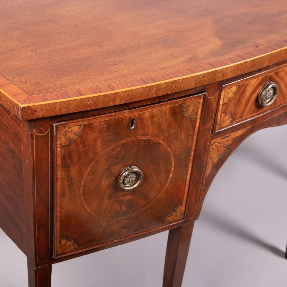 An 18th-century Georgian mahogany bow-fronted sideboard with satinwood inlays, central drawer, two flanking doors, and tapered square legs. View II