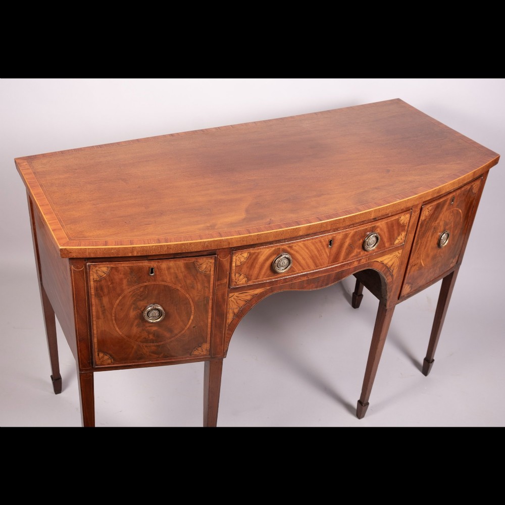 An 18th-century Georgian mahogany bow-fronted sideboard with satinwood inlays, central drawer, two flanking doors, and tapered square legs. View IV