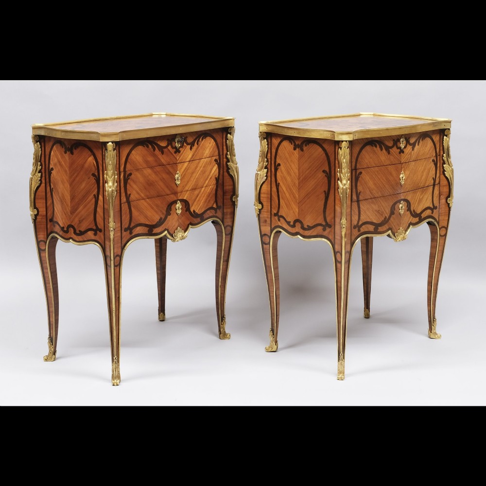 A pair of French Louis XV style inlaid timber commodes featuring serpentine fronts, marquetry veneering, cabriole legs, and chased gilt-bronze mounts.