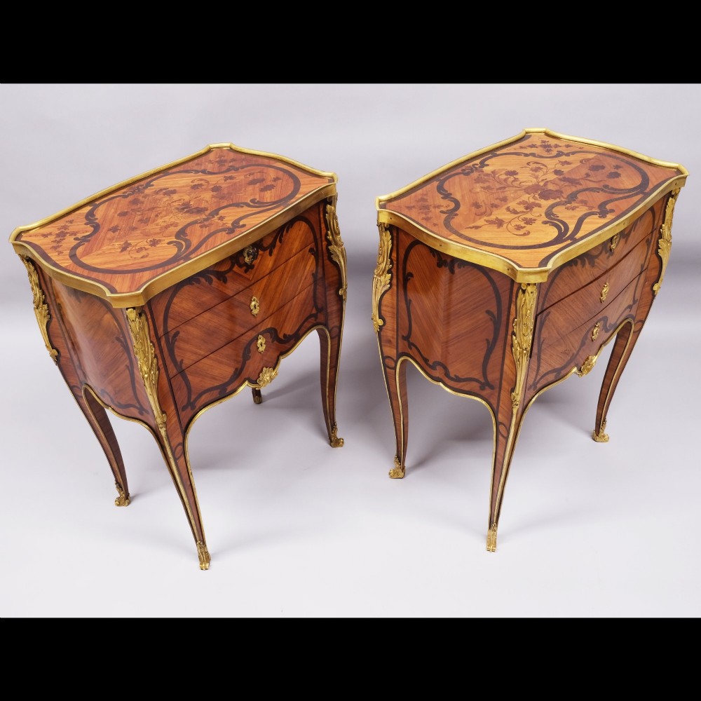 A pair of French Louis XV style inlaid timber commodes featuring serpentine fronts, marquetry veneering, cabriole legs, and chased gilt-bronze mounts. View V