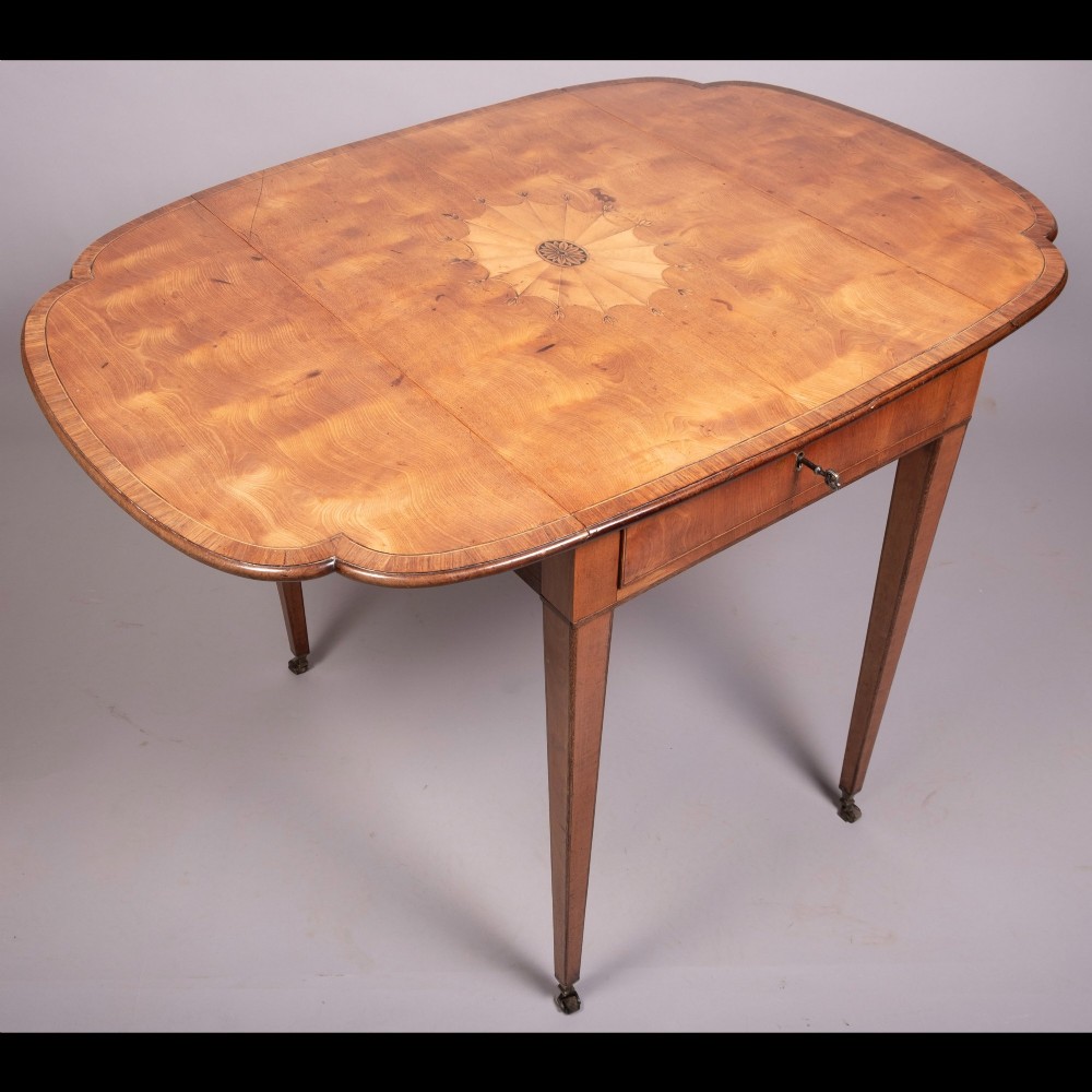 An 18th-century Georgian satinwood Pembroke table featuring extended drop leaves, a central fan marquetry inlay, crossbanded borders, a frieze drawer with key, and tapered legs ending in brass castors.