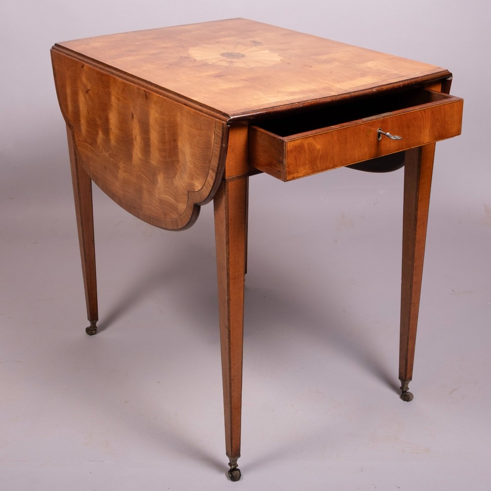 An 18th-century Georgian satinwood Pembroke table featuring extended drop leaves, a central fan marquetry inlay, crossbanded borders, a frieze drawer with key, and tapered legs ending in brass castors. View II