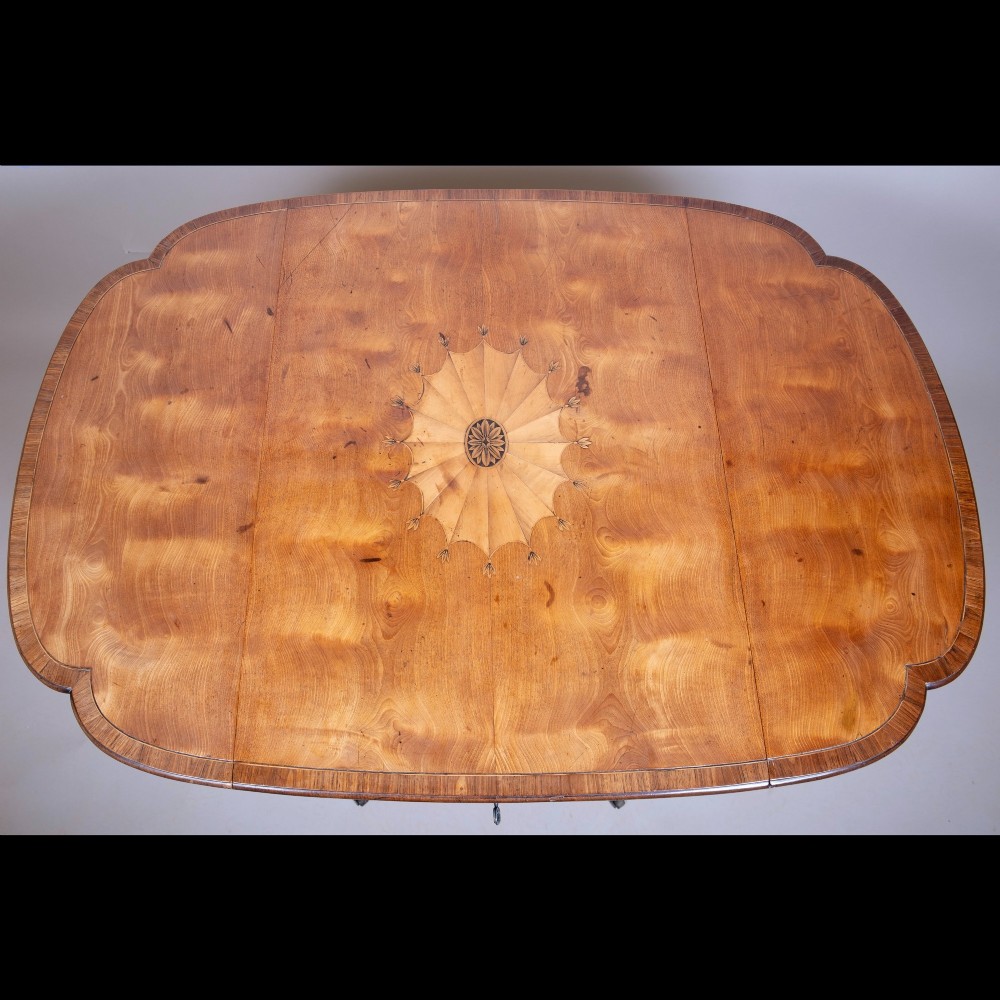 An 18th-century Georgian satinwood Pembroke table featuring extended drop leaves, a central fan marquetry inlay, crossbanded borders, a frieze drawer with key, and tapered legs ending in brass castors. View IV