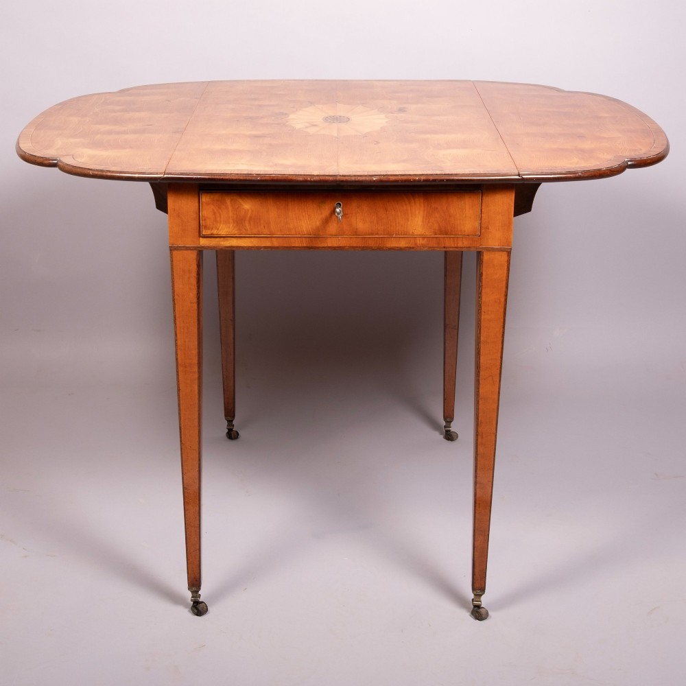 An 18th-century Georgian satinwood Pembroke table featuring extended drop leaves, a central fan marquetry inlay, crossbanded borders, a frieze drawer with key, and tapered legs ending in brass castors. View V