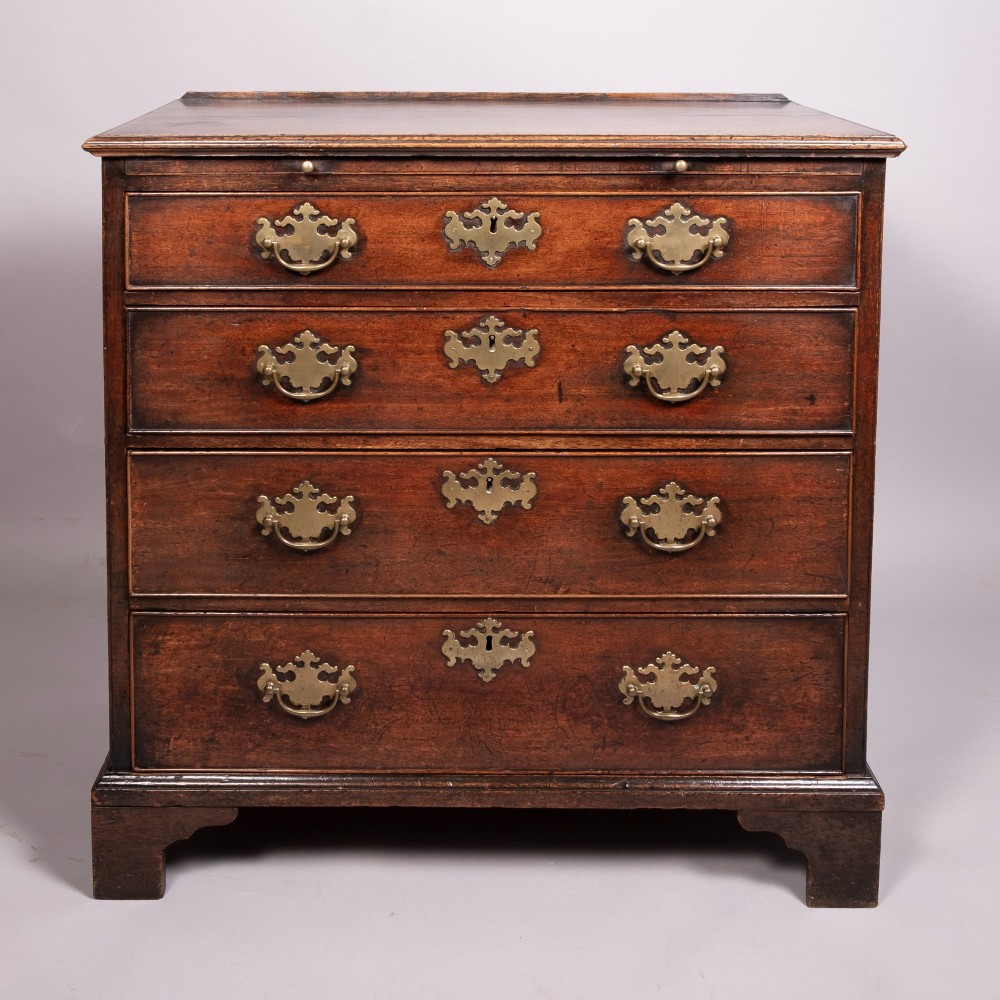 An 18th-century Georgian walnut chest of four drawers featuring brass swan-neck handles, pierced escutcheons, a brushing slide, and bracket feet.