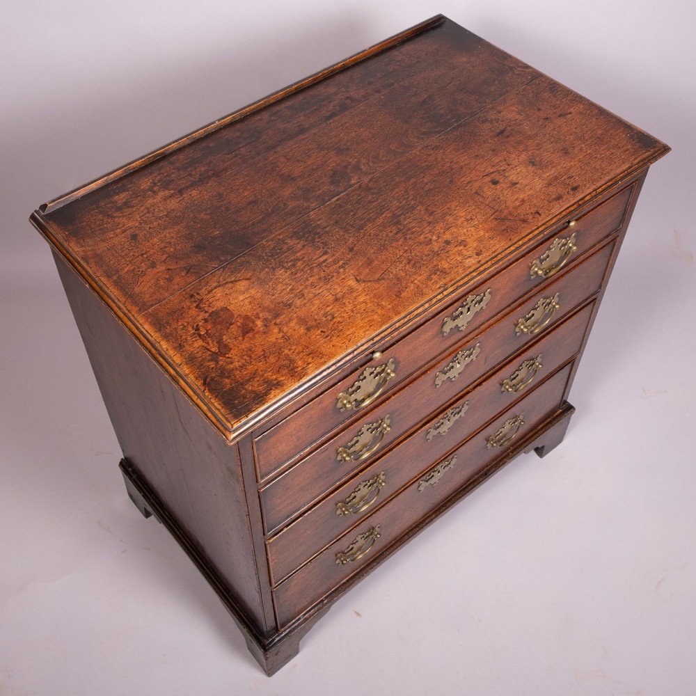 An 18th-century Georgian walnut chest of four drawers featuring brass swan-neck handles, pierced escutcheons, a brushing slide, and bracket feet. View II