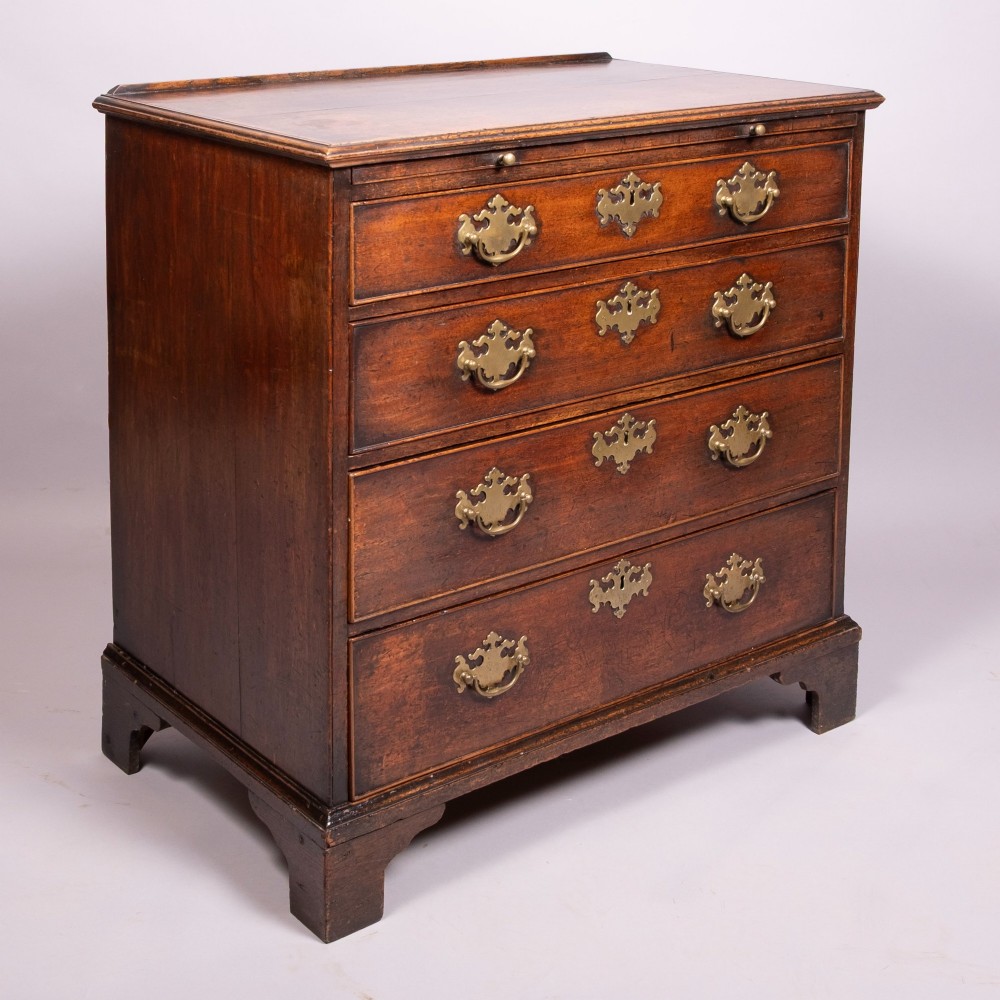 An 18th-century Georgian walnut chest of four drawers featuring brass swan-neck handles, pierced escutcheons, a brushing slide, and bracket feet. View III