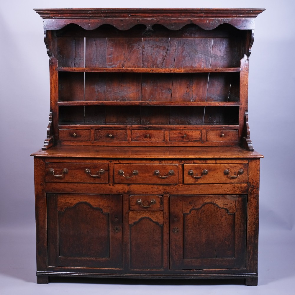 Mid 18th-century Welsh oak dresser with an open plate rack, scalloped top frieze, small spice drawers, and a base containing drawers and panelled cupboards.
