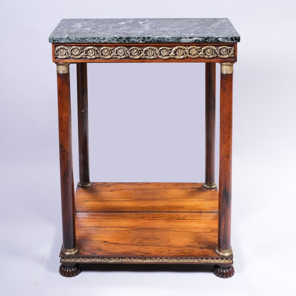 An antique First Empire rosewood console table featuring a dark green marble top, gilt brass mounts along the frieze, cylindrical column supports, and a lower shelf.