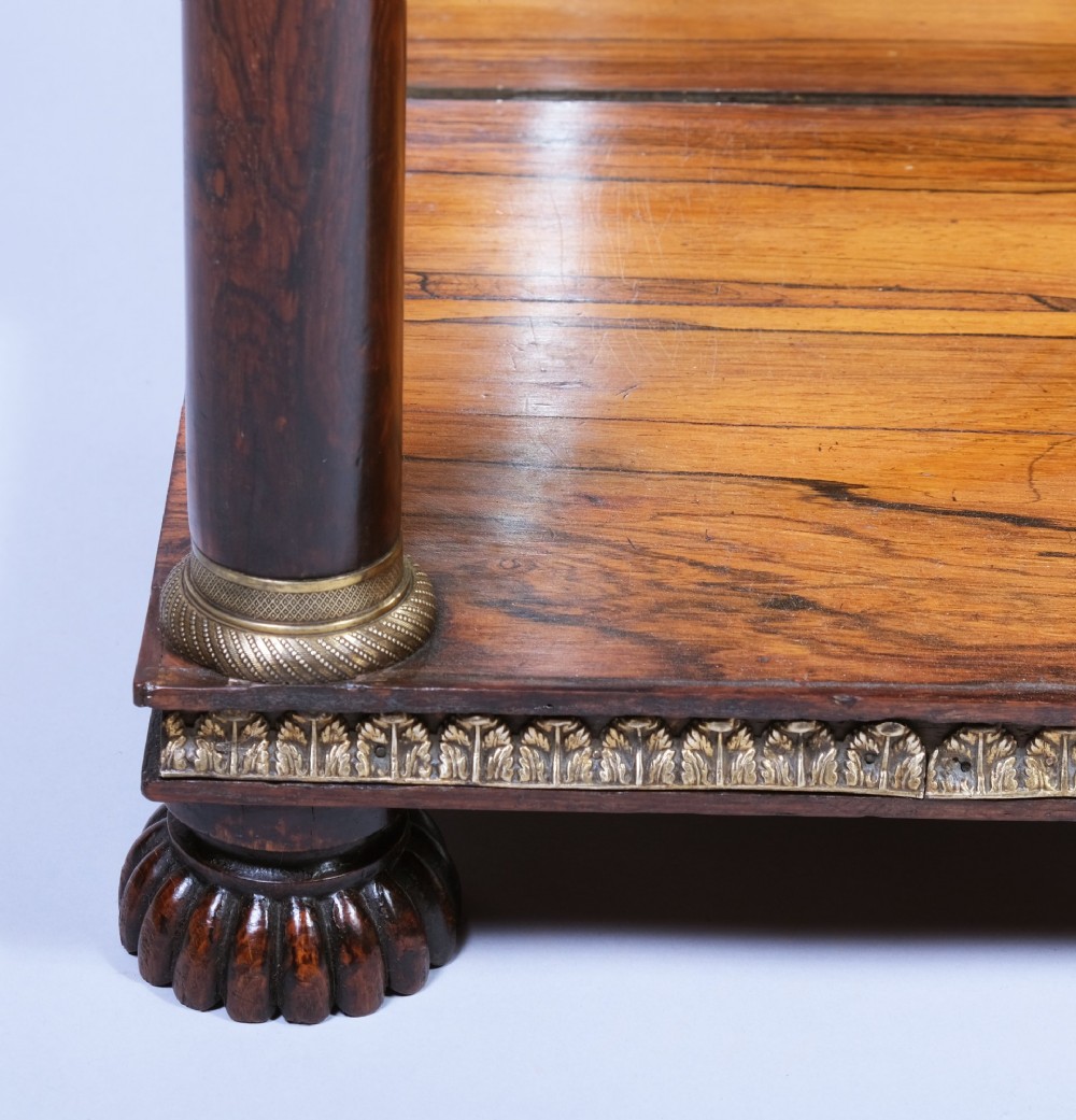 An antique First Empire rosewood console table featuring a dark green marble top, gilt brass mounts along the frieze, cylindrical column supports, and a lower shelf. View II