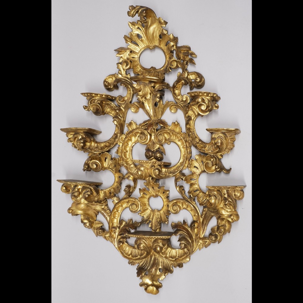 An ornate 19th-century carved giltwood wall bracket featuring C-scrolls, acanthus leaf motifs, and five display tiers against a light background.
