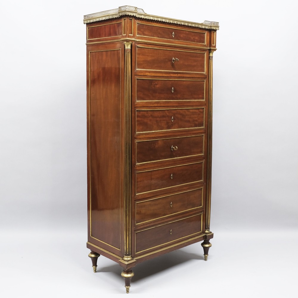 A tall mahogany semainier chest of drawers with seven brass-bordered drawer fronts, corner pilasters, and a brass gallery top.