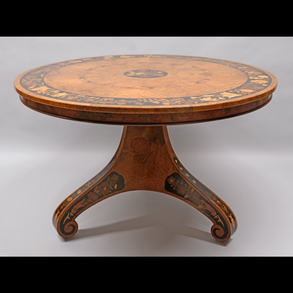 A 19th-century circular burr walnut centre table featuring elaborate floral marquetry inlay along the top border, central medallion, and tri-form pedestal base.