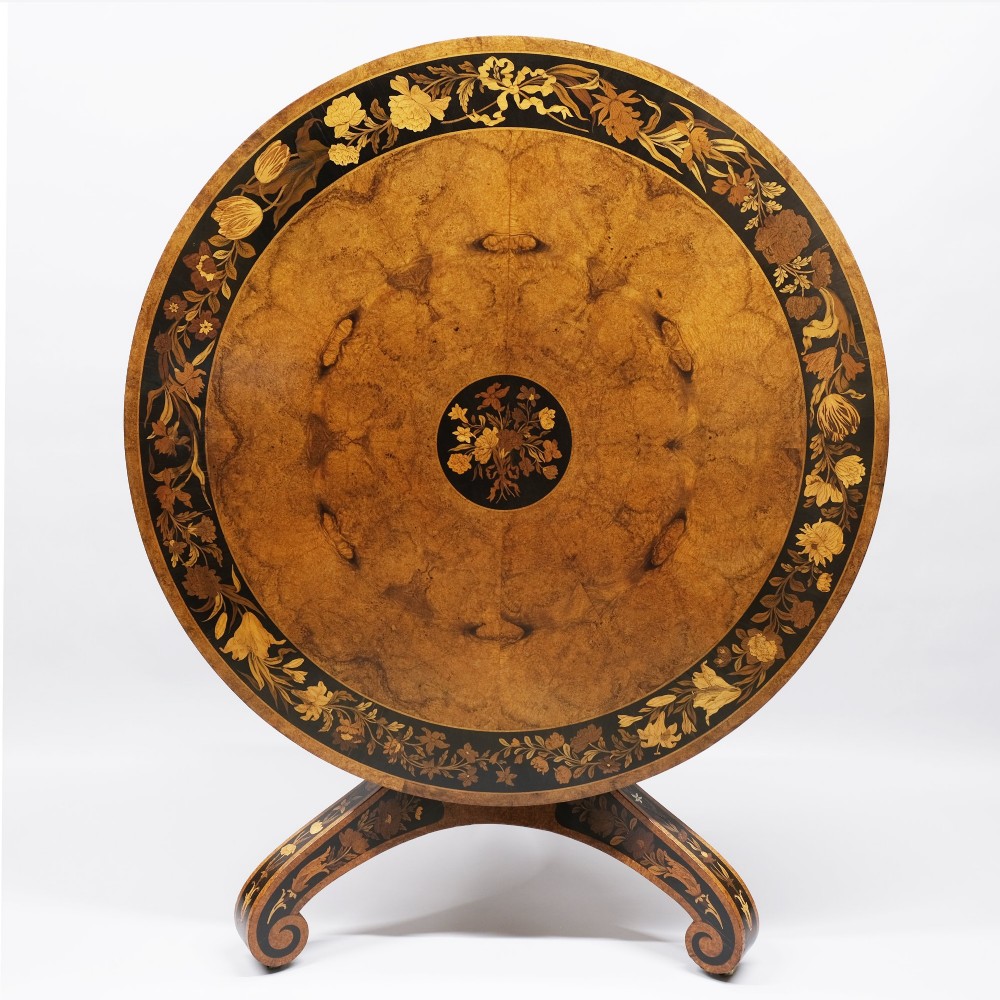 A 19th-century circular burr walnut centre table featuring elaborate floral marquetry inlay along the top border, central medallion, and tri-form pedestal base. View II