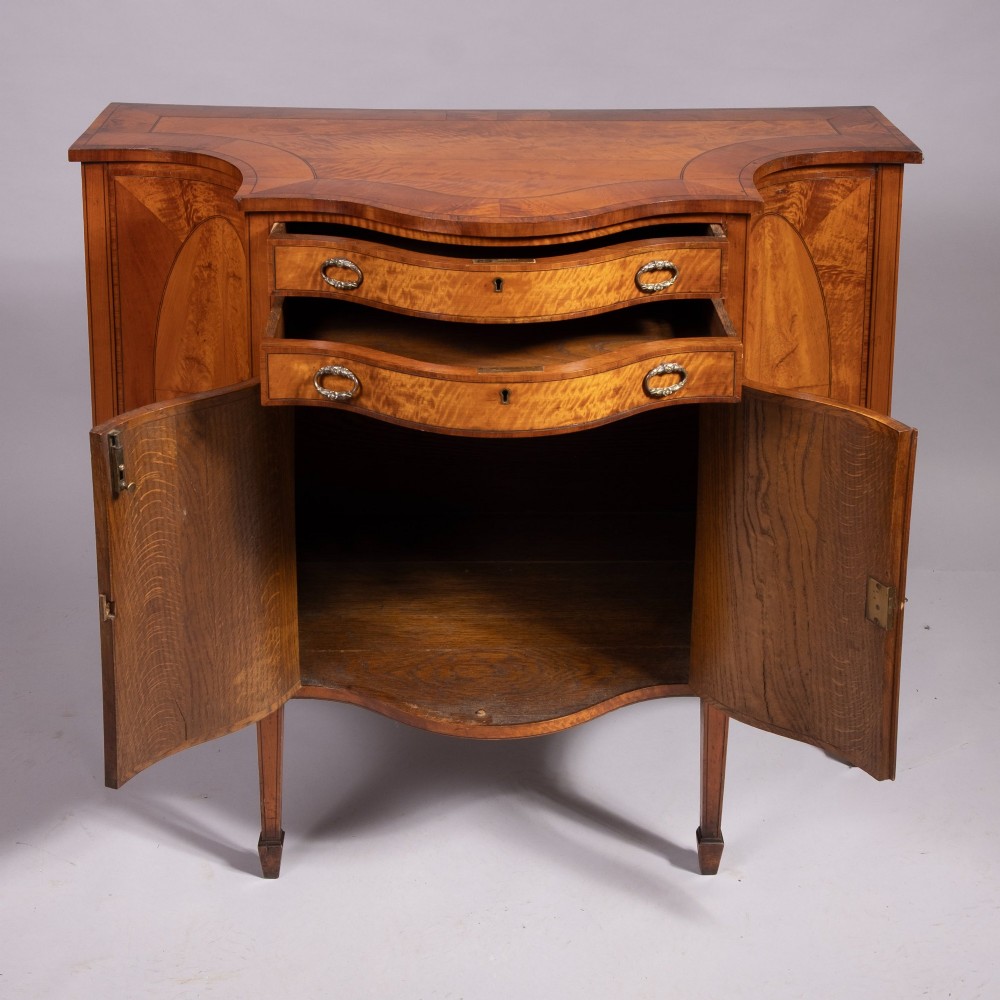 A Sheraton Revival satinwood side cabinet featuring bow-fronted drawers, inlaid oval door panels, and tapered square legs. View II