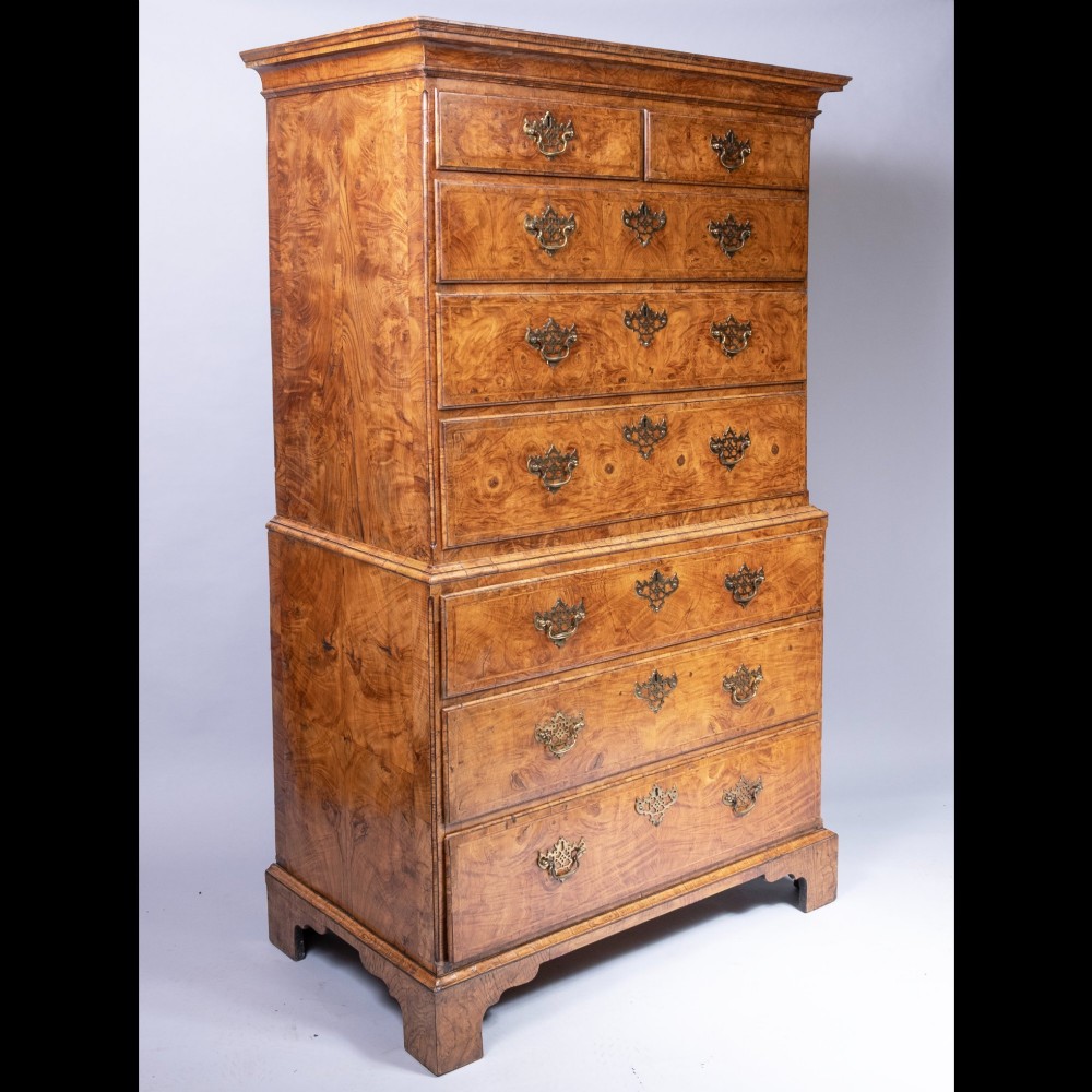 An early eighteenth-century George I elm tallboy chest-on-chest featuring two sections with multiple graduating drawers and decorative brass handles set on bracket feet.