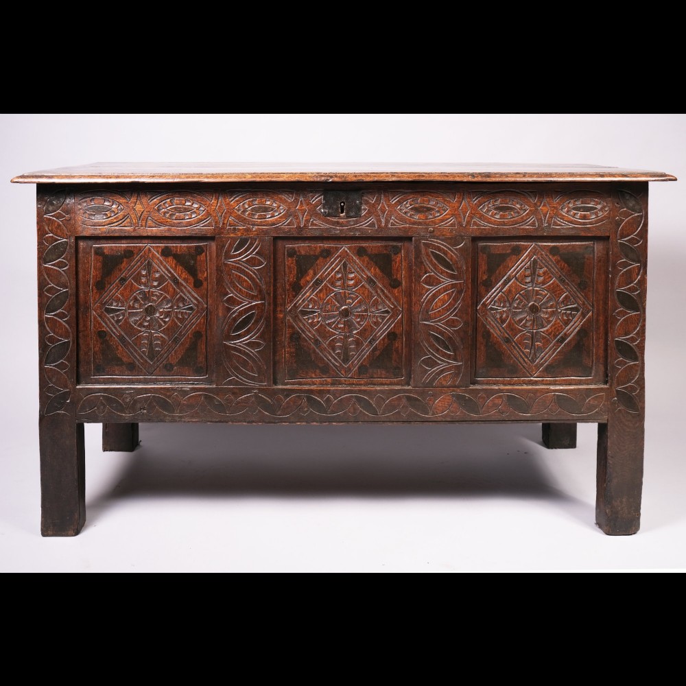 A 17th-century dark oak coffer with carved lozenge panels and a flat hinged top.