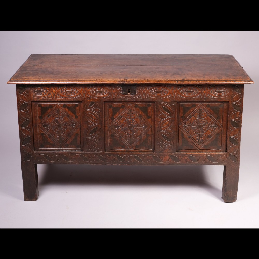 A 17th-century dark oak coffer with carved lozenge panels and a flat hinged top. View II