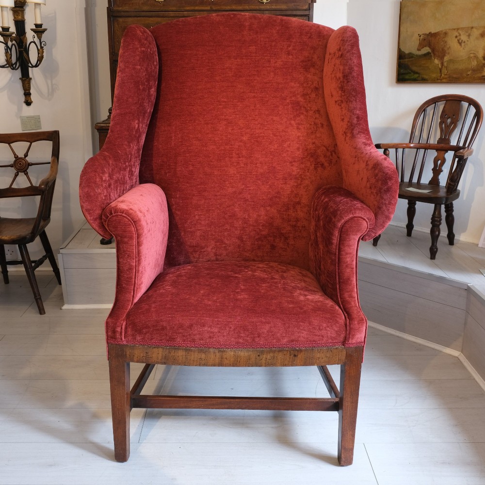 A late 19th-century wingback armchair upholstered in rich red velvet with square timber legs and a stretcher base.