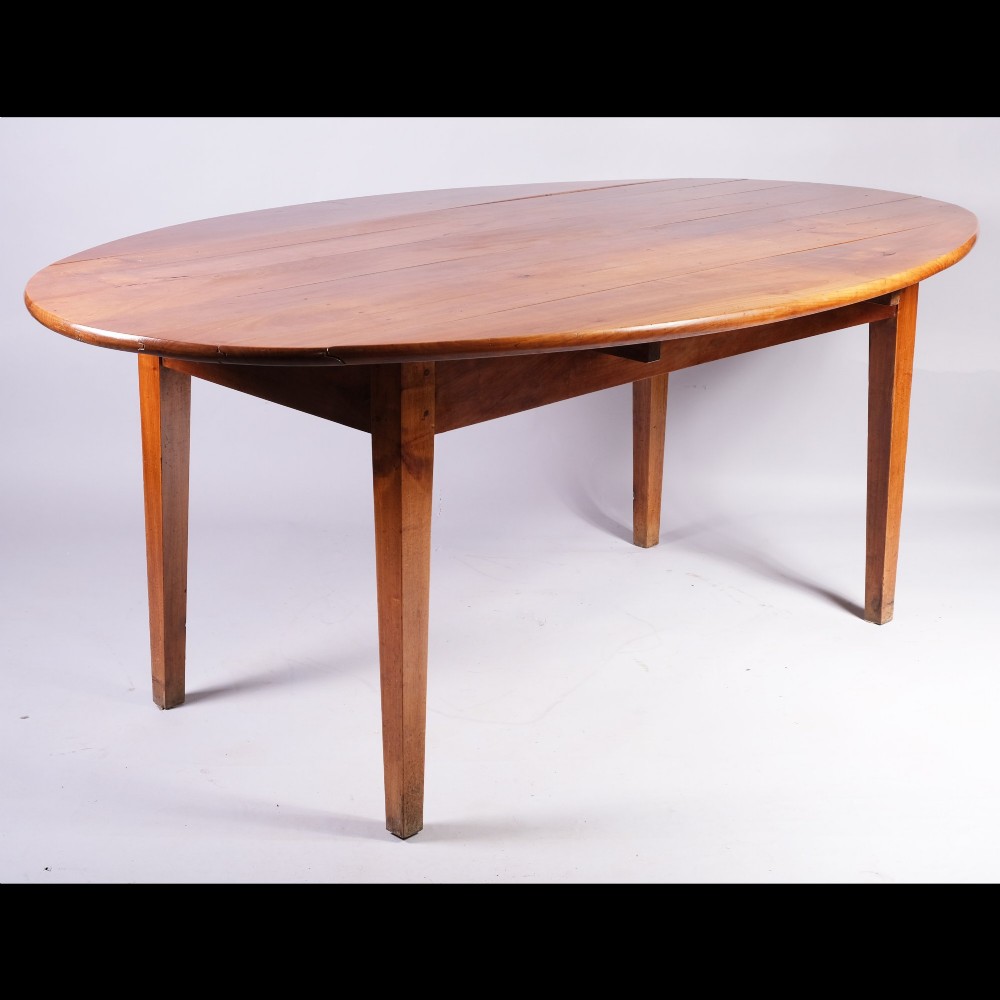 A nineteenth-century French oval dining table crafted from warm brown cherrywood with four tapered square legs.