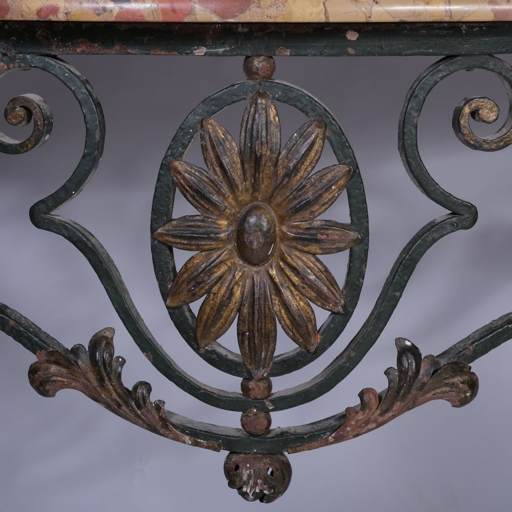 A 19th-century serpentine console table featuring a contoured marble top resting on a dark green wrought iron frame decorated with floral rosettes and scrollwork. View IV