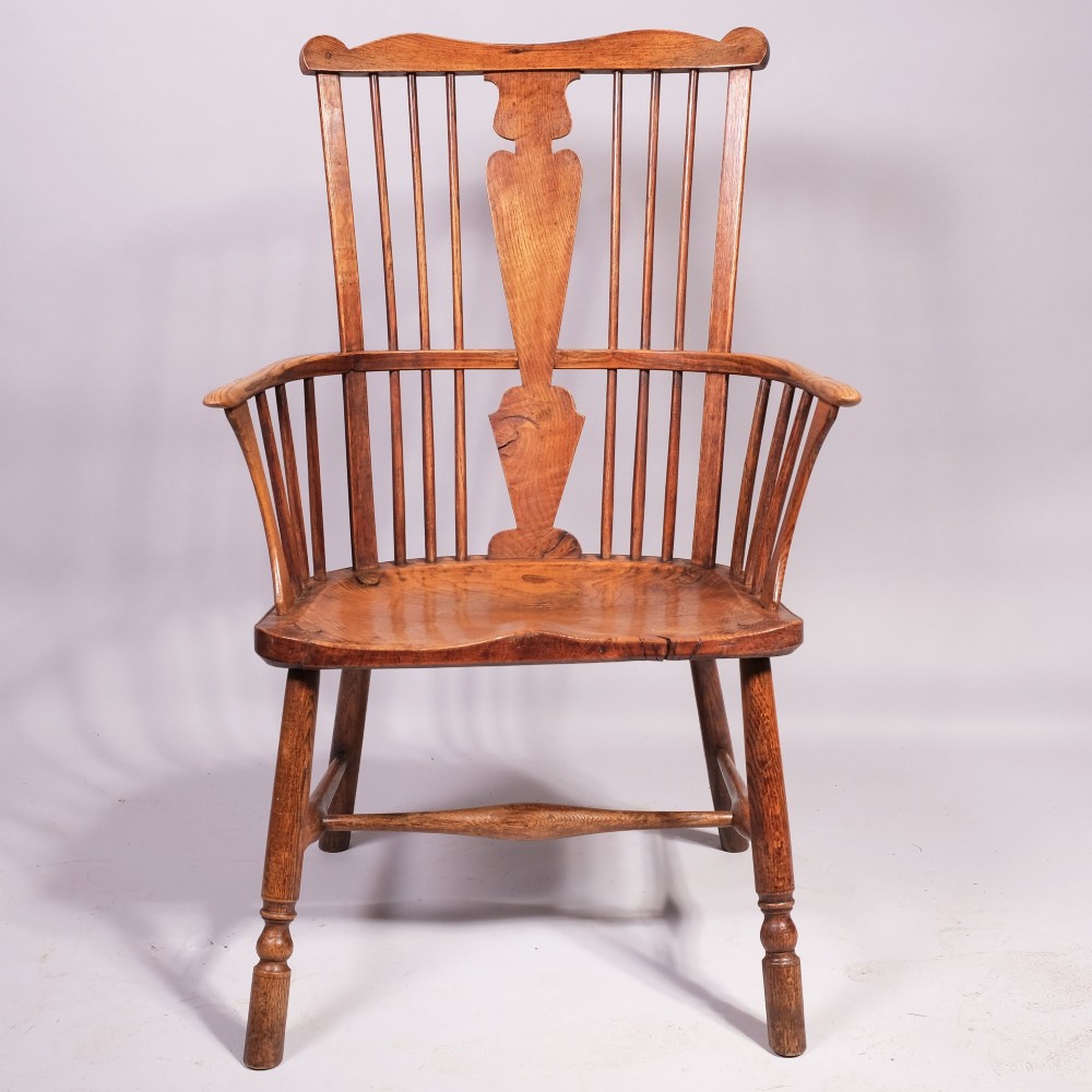 An eighteenth-century ash comb back Windsor armchair featuring a shaped crest rail, vertical spindles, a central vase splat, contoured wooden seat, and turned legs.