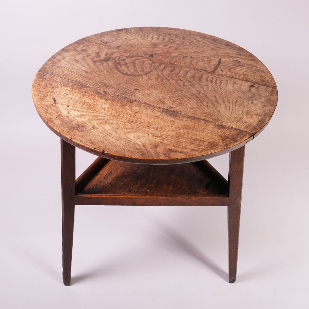An 18th-century ash wood cricket table featuring a round top, three straight tapered legs, and a triangular lower shelf in a warm brown finish. View II