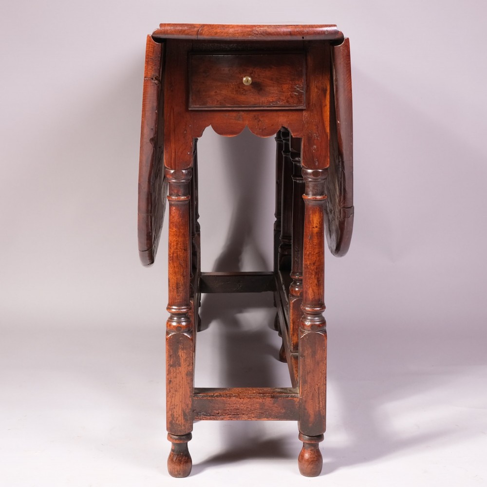An 18th-century yew wood gateleg table featuring an oval drop-leaf top, turned legs, lower stretchers, and a single end drawer with a brass knob. View II