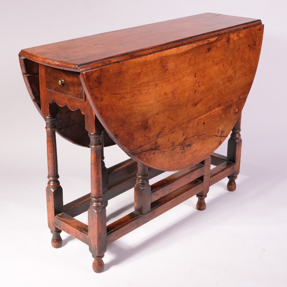 An 18th-century yew wood gateleg table featuring an oval drop-leaf top, turned legs, lower stretchers, and a single end drawer with a brass knob. View IV