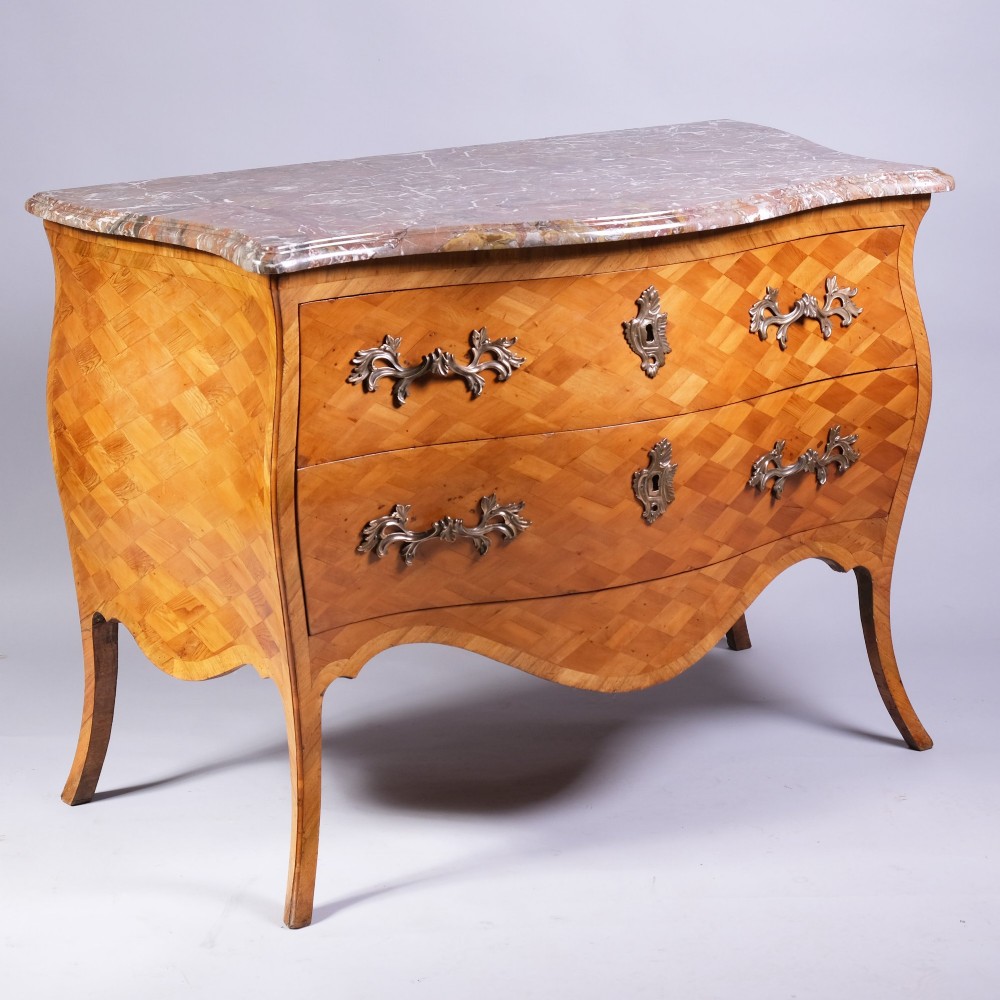 A French bombe commode featuring geometric parquetry wood veneer, two deep drawers with cast metal handles, cabriole legs, and a fitted grey veined marble top.