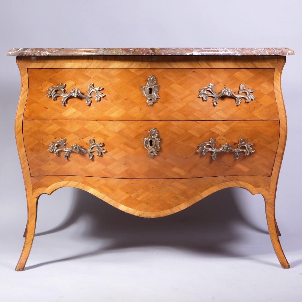 A French bombe commode featuring geometric parquetry wood veneer, two deep drawers with cast metal handles, cabriole legs, and a fitted grey veined marble top. View IV