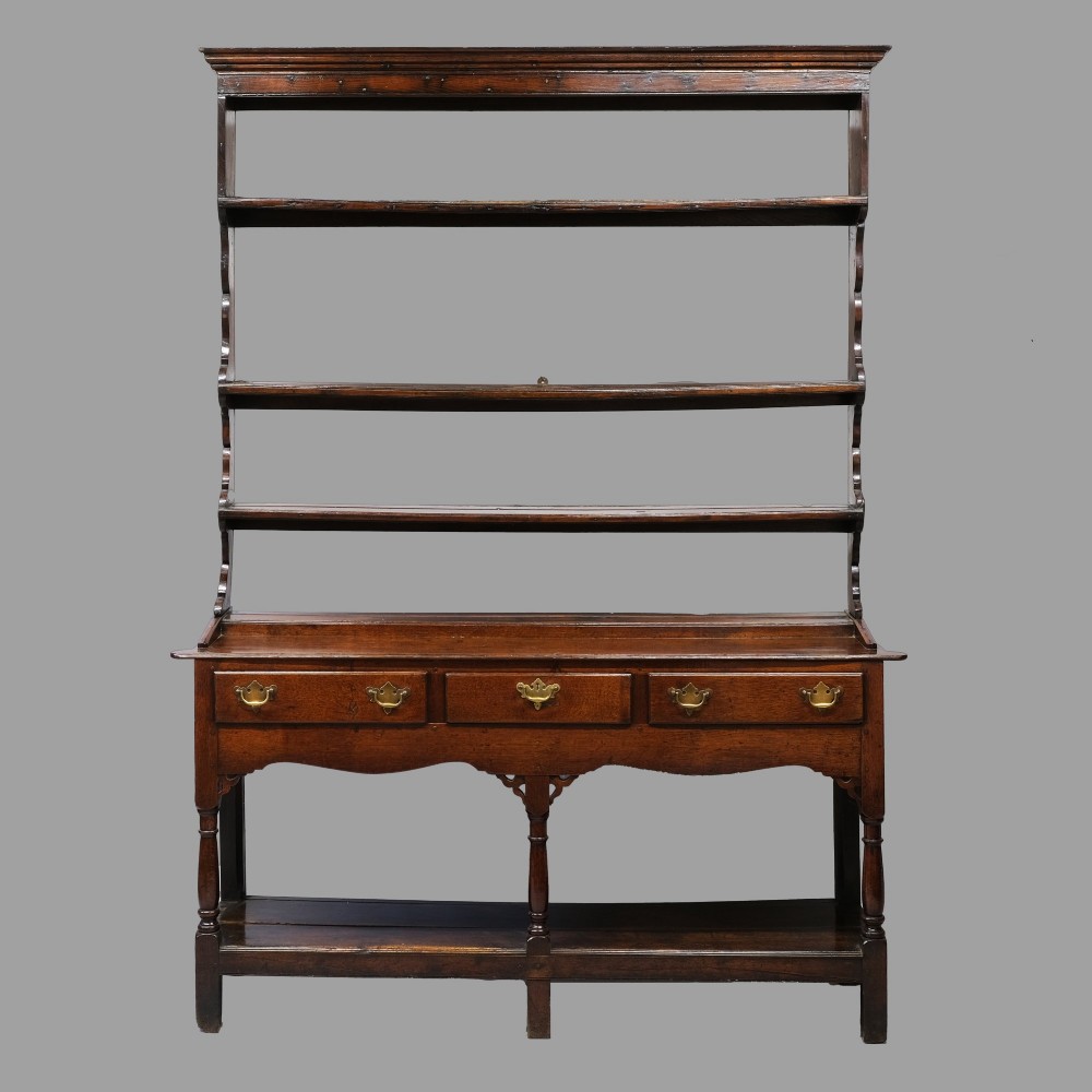 An 18th-century dark oak Welsh potboard dresser featuring an upper three-tier plate rack above three drawers with brass handles and a low open shelf.