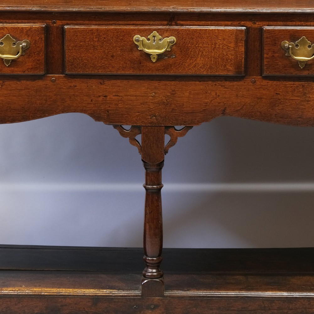 An 18th-century dark oak Welsh potboard dresser featuring an upper three-tier plate rack above three drawers with brass handles and a low open shelf. View II