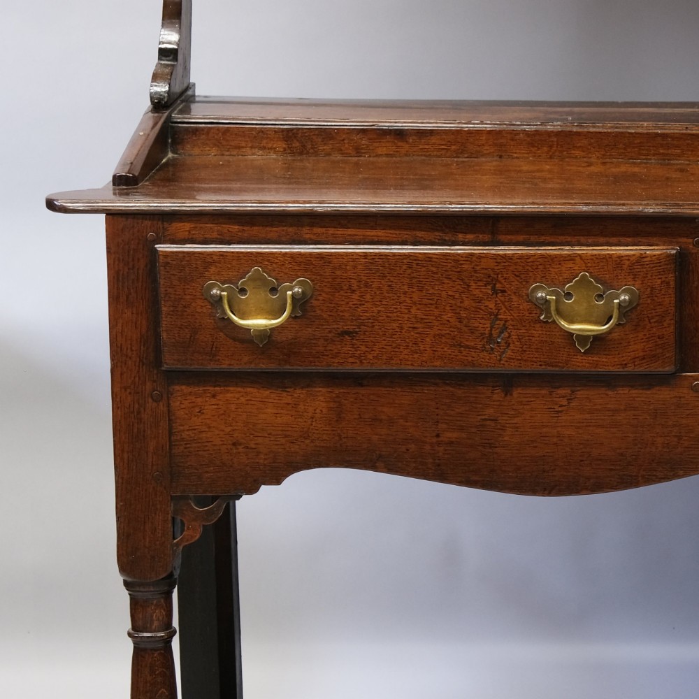 An 18th-century dark oak Welsh potboard dresser featuring an upper three-tier plate rack above three drawers with brass handles and a low open shelf. View III