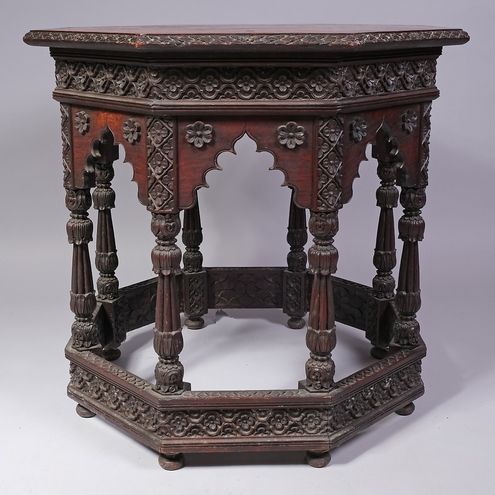 A 19th-century octagonal dark hardwood table featuring deeply carved floral borders, cusped arch aprons, turned multi-baluster legs, and a fitted base shelf.
