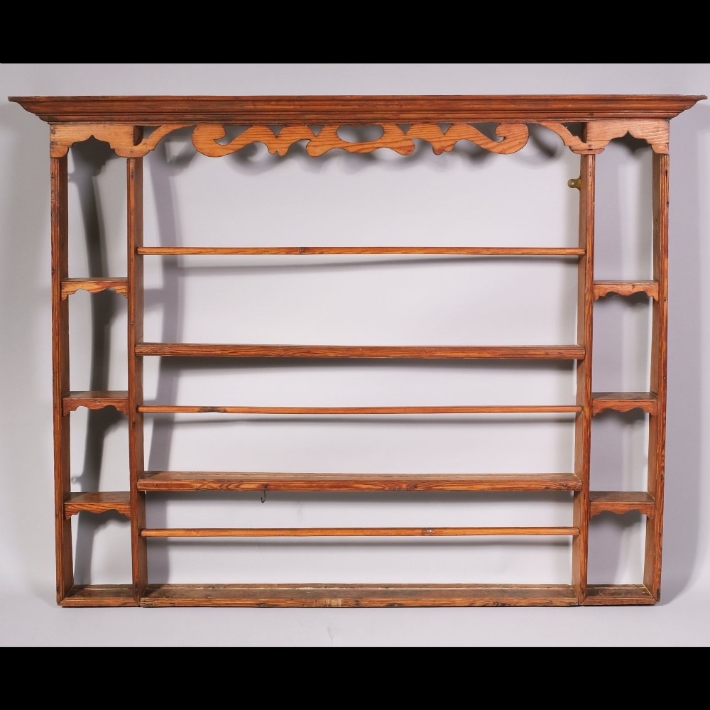 An 18th-century wall-mounted pine plate rack featuring a moulded cornice, decorative fretwork top frieze, open tiered shelves with retaining bars, and side alcoves.