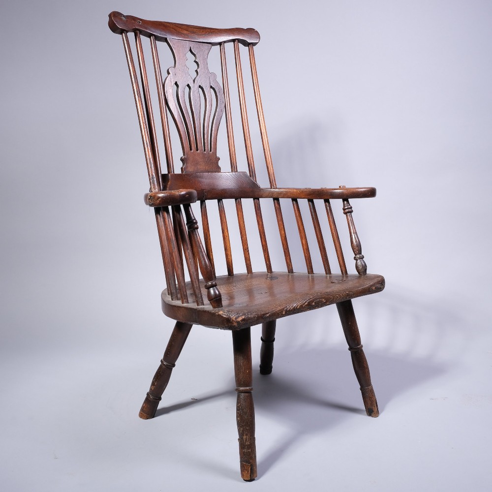 A mid 18th-century dark timber comb-back Windsor armchair with turned legs, a contoured solid seat, and a central pierced back splat.
