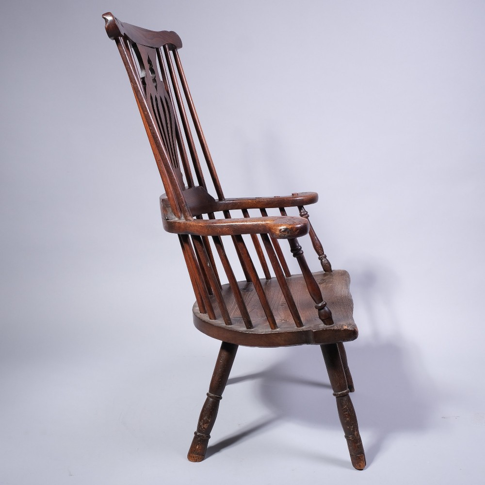 A mid 18th-century dark timber comb-back Windsor armchair with turned legs, a contoured solid seat, and a central pierced back splat. View II