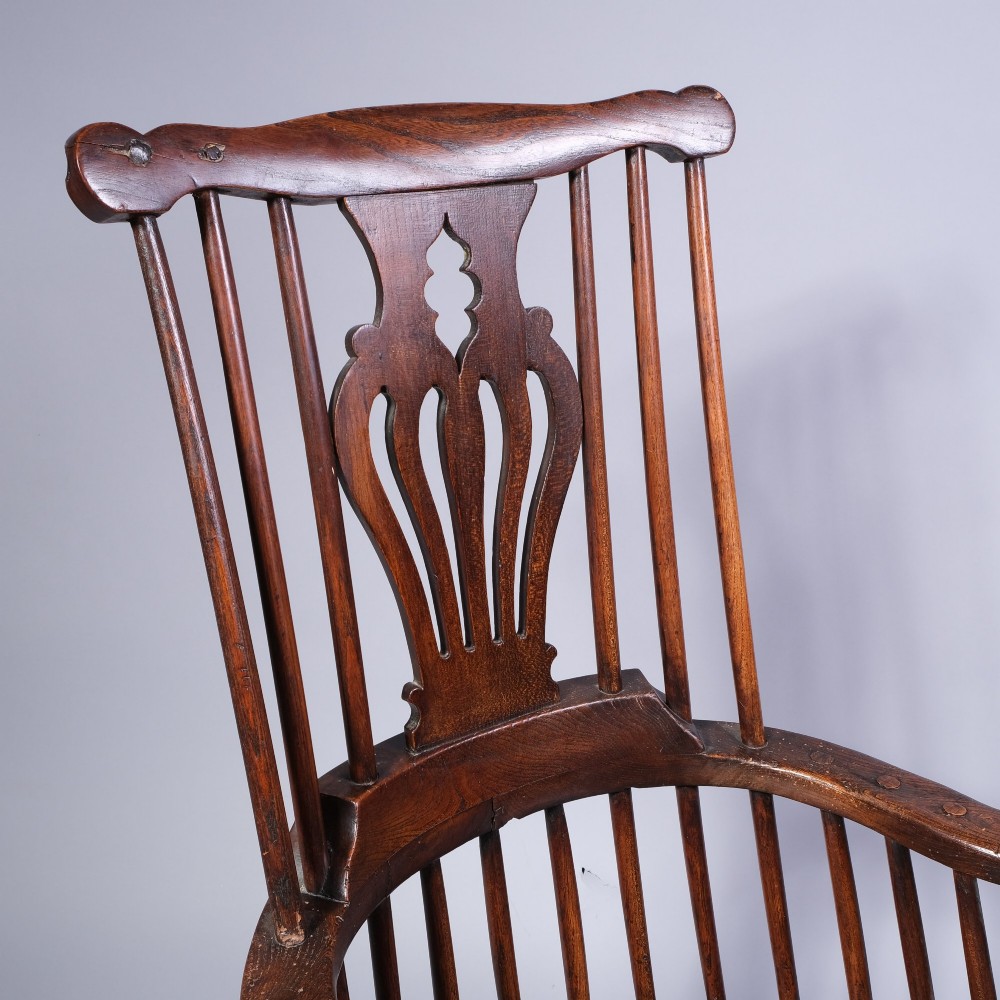 A mid 18th-century dark timber comb-back Windsor armchair with turned legs, a contoured solid seat, and a central pierced back splat. View III