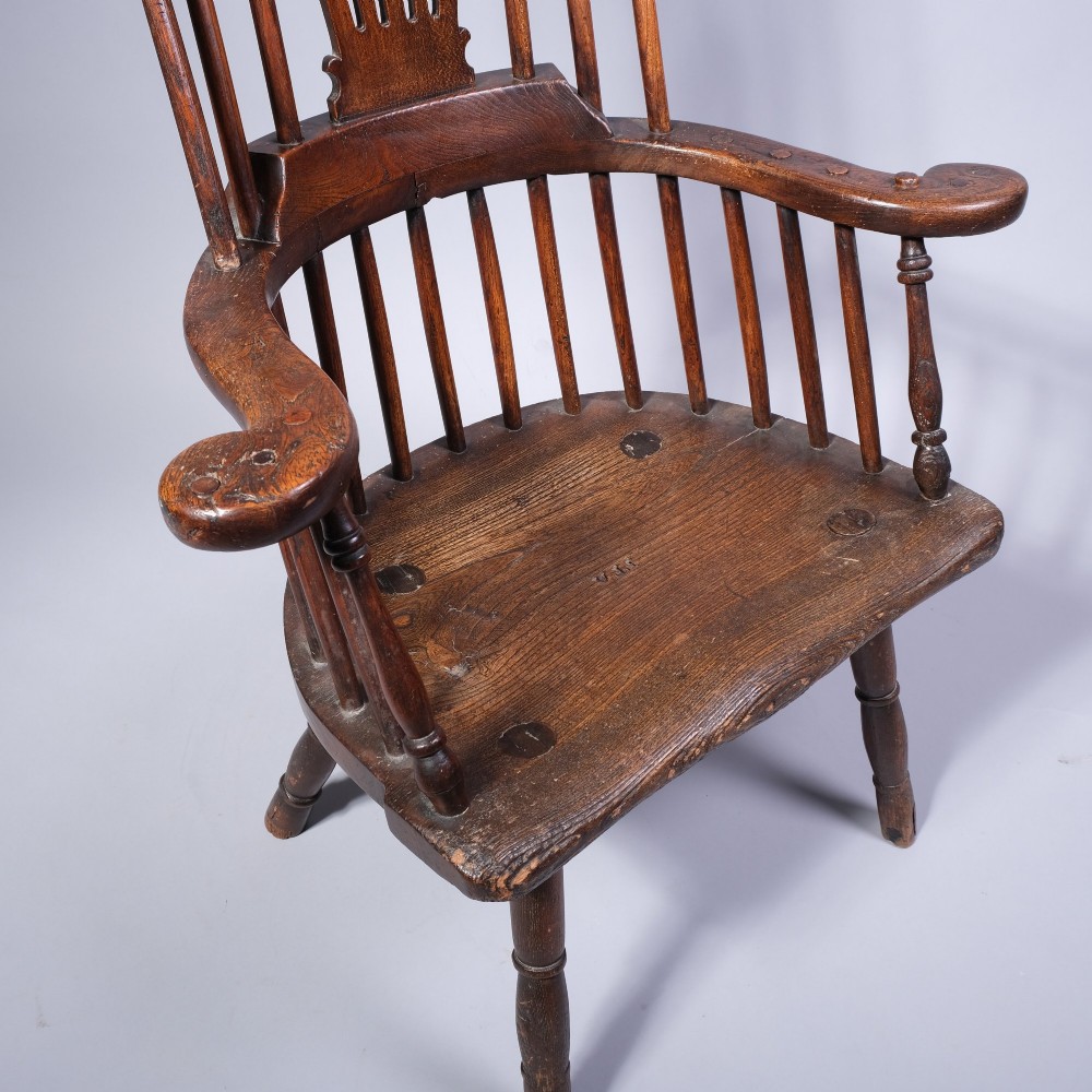 A mid 18th-century dark timber comb-back Windsor armchair with turned legs, a contoured solid seat, and a central pierced back splat. View IV