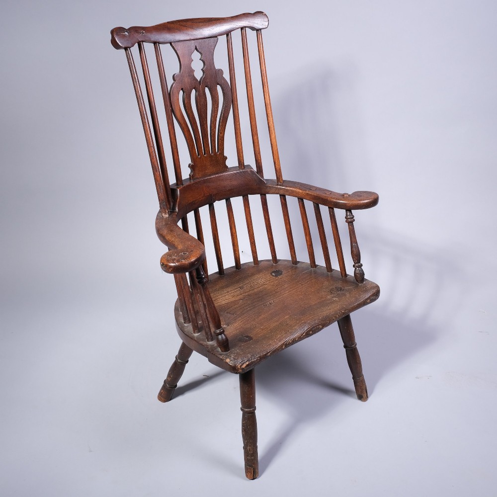 A mid 18th-century dark timber comb-back Windsor armchair with turned legs, a contoured solid seat, and a central pierced back splat. View V