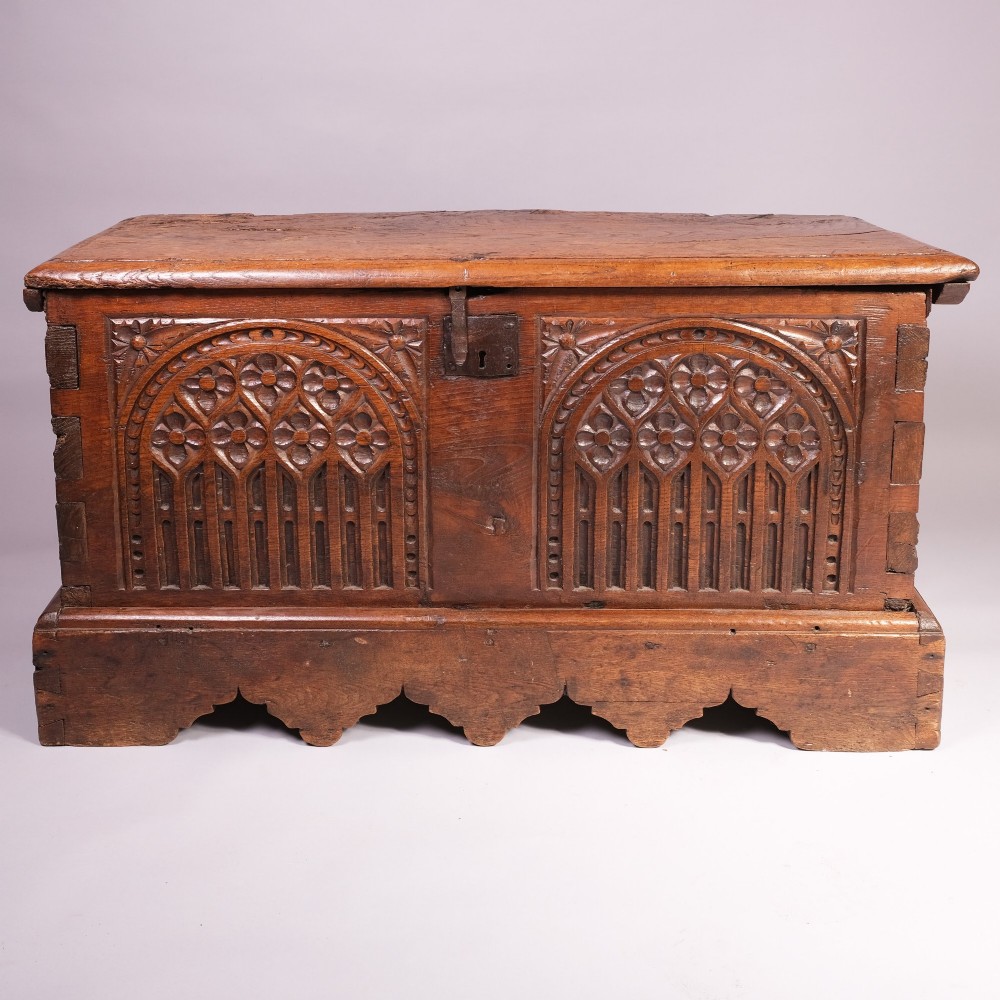 An antique oak and elm coffer featuring carved Gothic tracery arches across the front panel and a hand-forged iron lockplate.