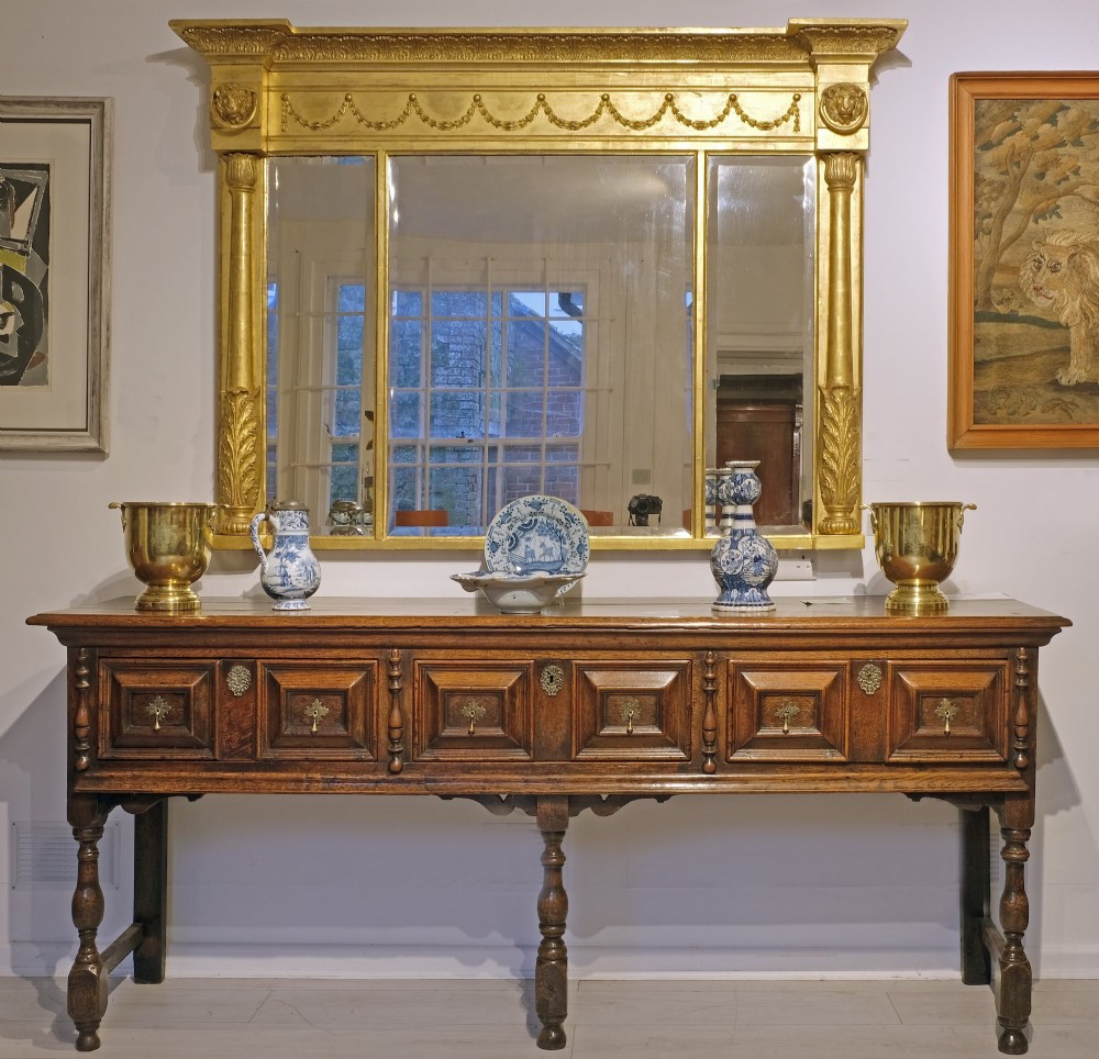 Late 17th-century oak dresser base featuring geometric panelled drawer fronts, brass drop handles, keyhole escutcheons, and turned legs with stretchers.