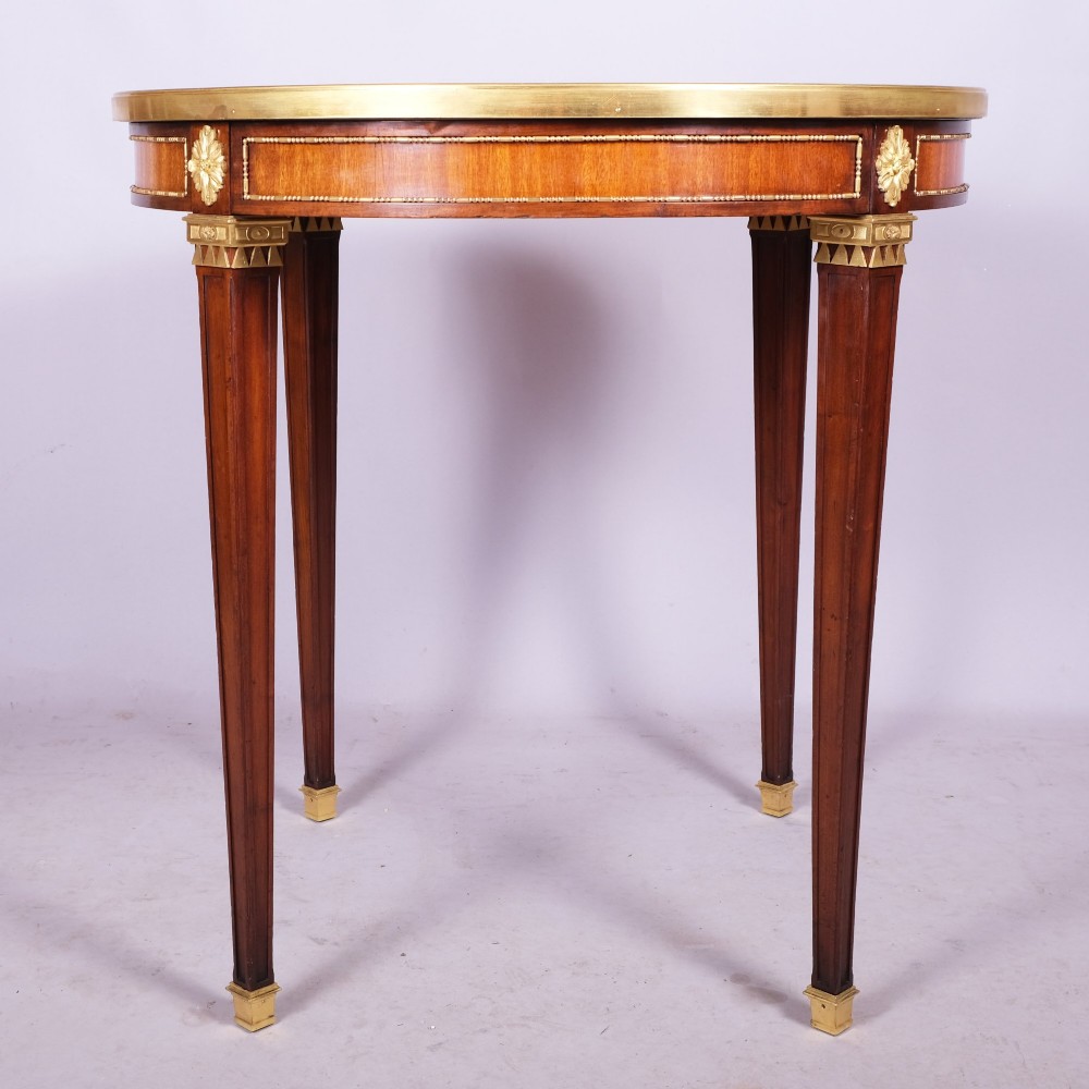A late 19th-century French Louis XVI style circular bouillotte table featuring a marble top with brass gallery rim, mahogany frieze with gilt mounts, and four square tapered legs.