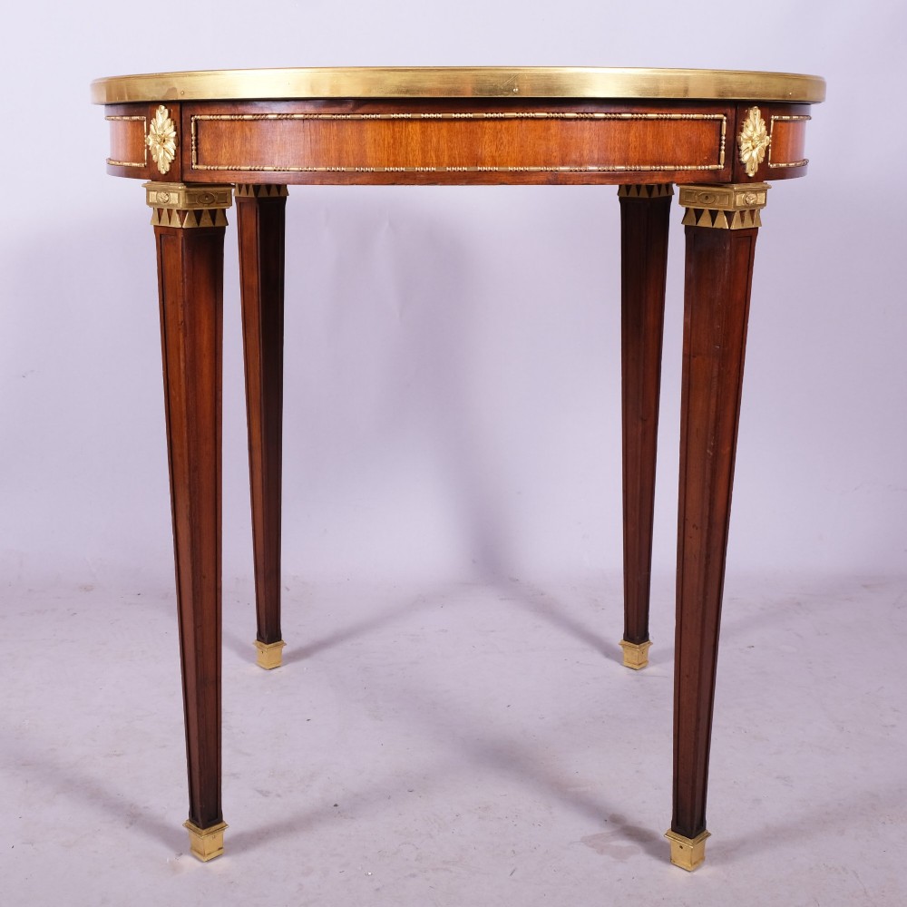 A late 19th-century French Louis XVI style circular bouillotte table featuring a marble top with brass gallery rim, mahogany frieze with gilt mounts, and four square tapered legs. View IV