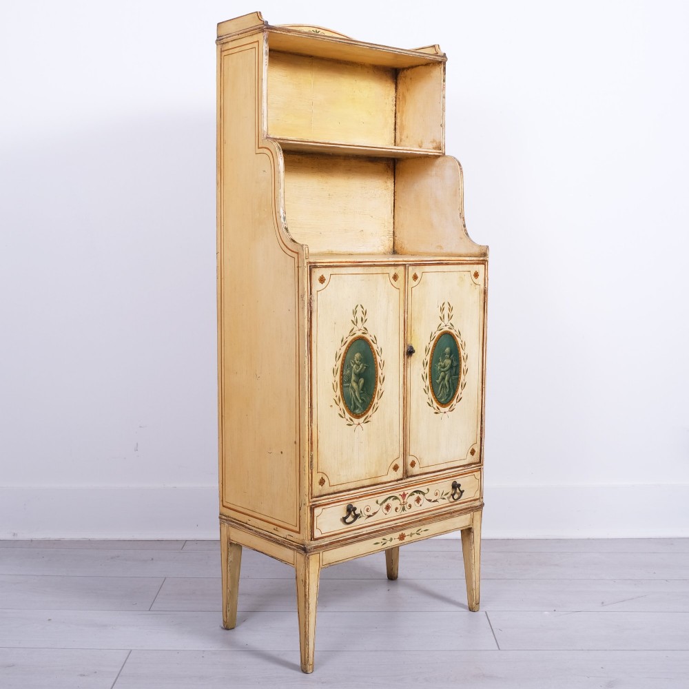 A late 18th-century George III painted waterfall bookcase featuring tiered open shelves above a two-door cabinet with green painted medallions and a single drawer on tapered legs.