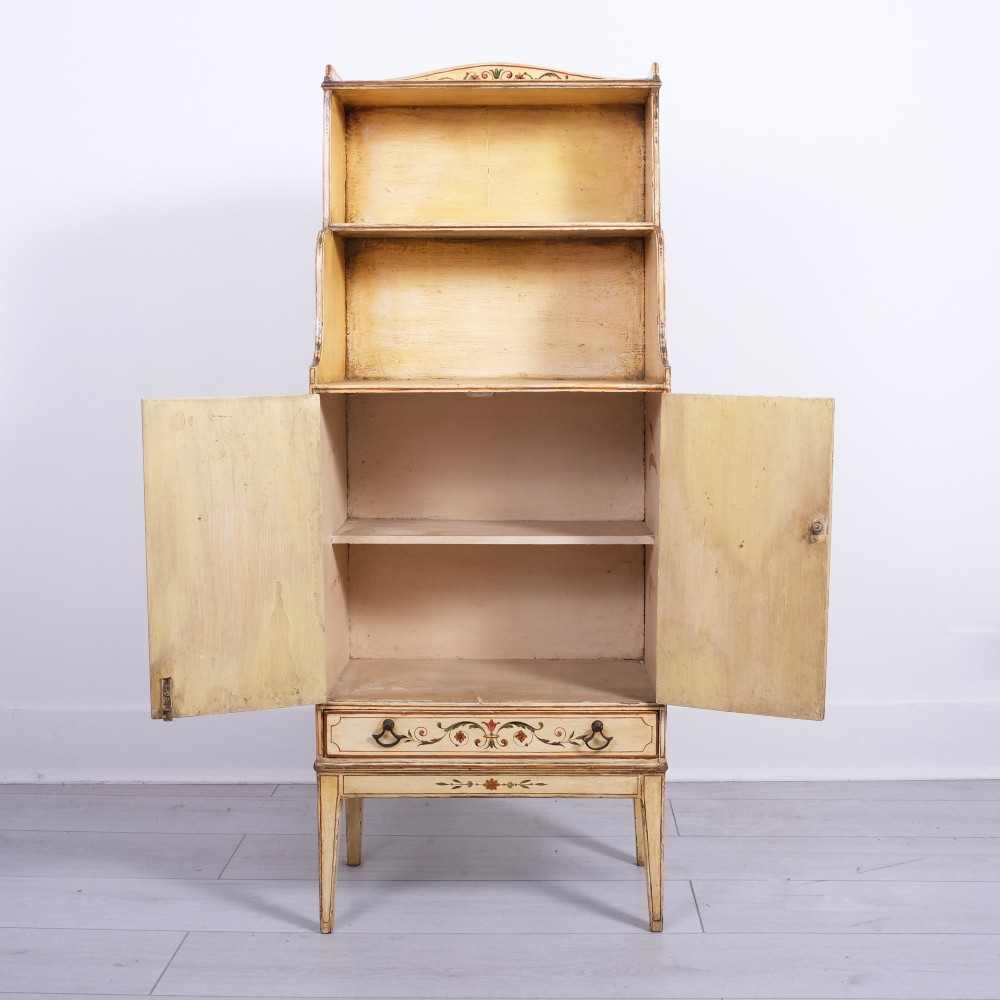 A late 18th-century George III painted waterfall bookcase featuring tiered open shelves above a two-door cabinet with green painted medallions and a single drawer on tapered legs. View III