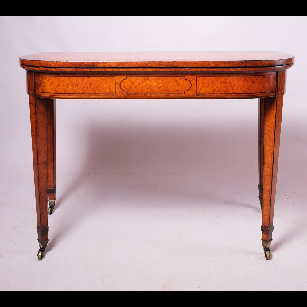 A late eighteenth-century Georgian amboyna fold-over tea table featuring string inlay, a rectangular apron with a central cartouche panel, and square tapered legs on brass castors.