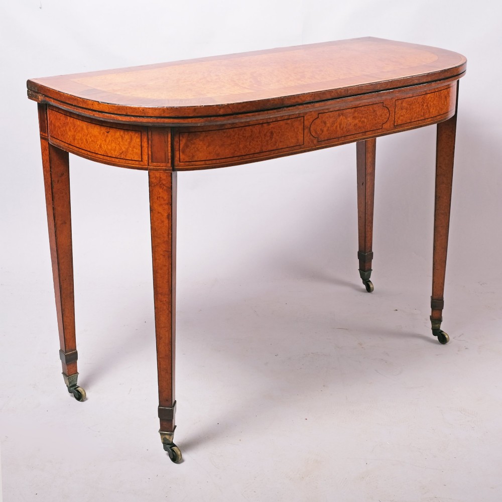 A late eighteenth-century Georgian amboyna fold-over tea table featuring string inlay, a rectangular apron with a central cartouche panel, and square tapered legs on brass castors. View III
