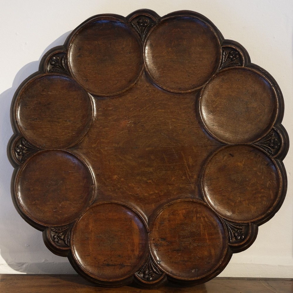A circular carved dark oak lazy susan featuring eight recessed round dish compartments surrounding a central tray with carved floral rim accents.